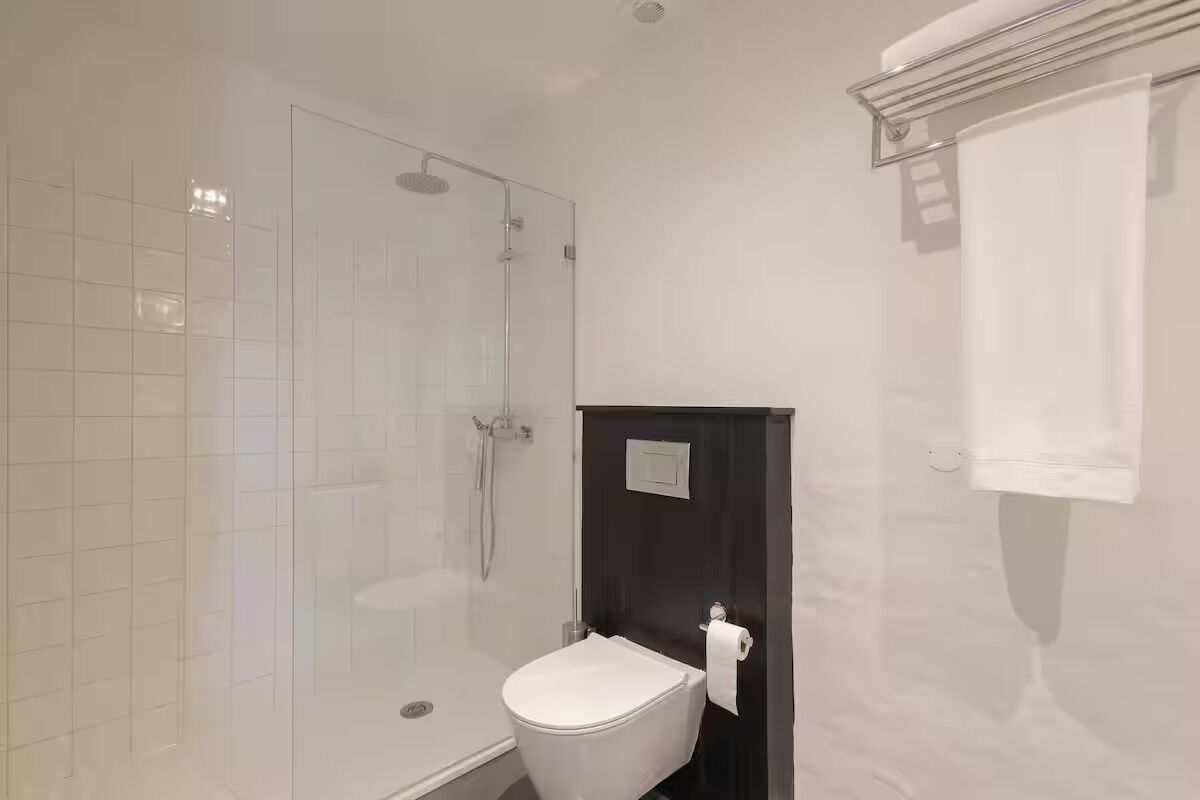 Une salle de bain moderne avec une douche à parois de verre, des toilettes blanches et une porte en bois foncé.