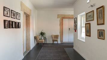 A hallway with framed photographs on the walls, a rug, two chairs, and a door at the end.