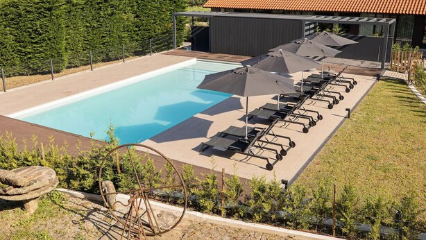 A swimming pool with lounge chairs and umbrellas, surrounded by greenery and a building with a tiled roof. - Tranquil Rural Getaway with Pool Access and Rustic Atmosphere - Near Braga (Braga)
