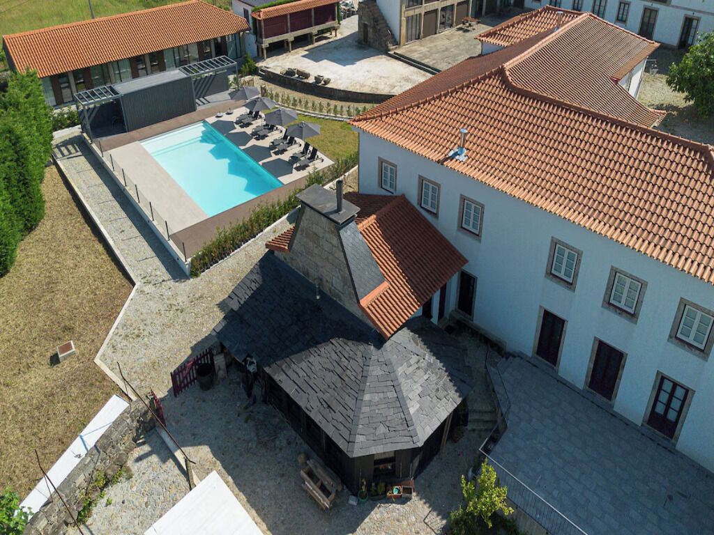 Vista aérea de una propiedad con piscina, un porche cubierto y un edificio con tejado de baldosas.