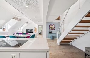 A modern kitchen with a central island, a dining area with teal chairs, and a staircase with wooden steps. - AN EXCEPTIONAL BLEND OF ELEGANCE, COMFORT WITH BREATHTAKING ROOFTOP TERRACES (Zürich)