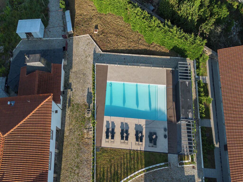 Vista aérea de un área de piscina con una pileta rectangular, tumbonas y un espacio de estar techado.