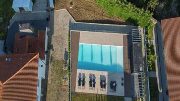 Vista aérea de un área de piscina con una pileta rectangular, tumbonas y un espacio de estar techado.