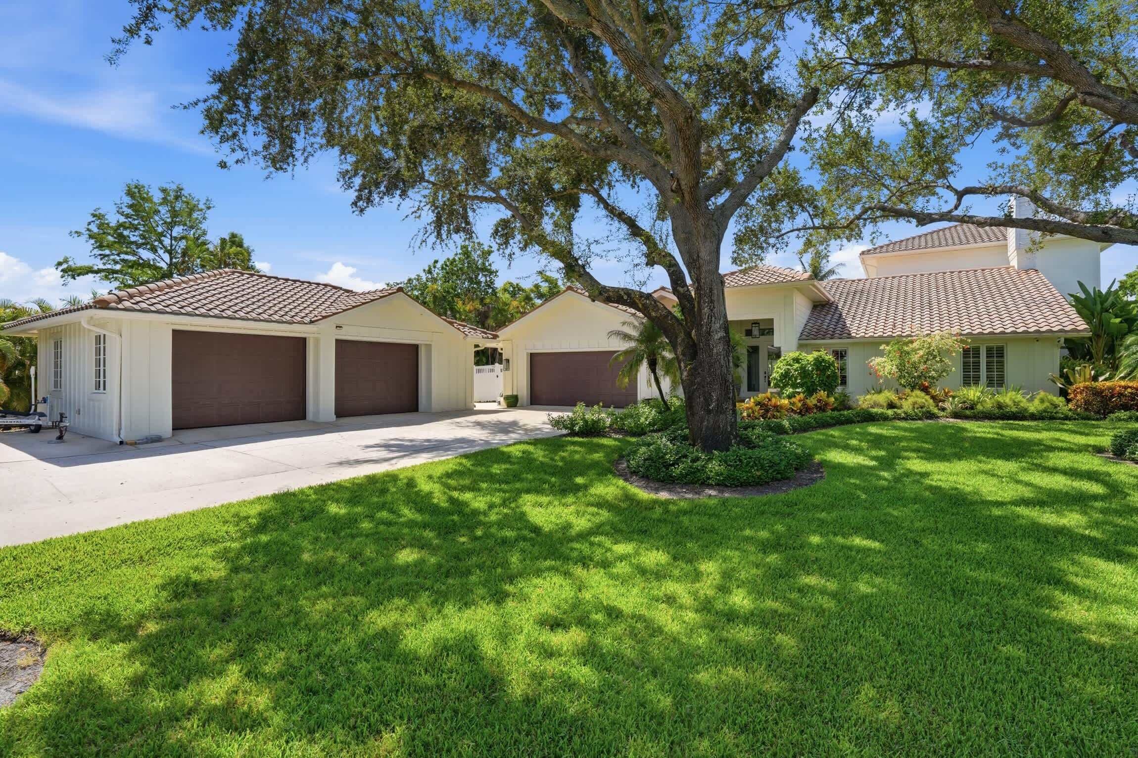 A residential property with a driveway, a large tree, and a well-maintained lawn.