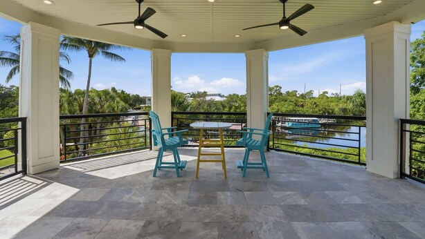 A covered outdoor seating area with two chairs and a table, a ceiling fan, and a view of a lake and greenery. - Riverfront Retreat with Pool, Spa & Dock (Estero)