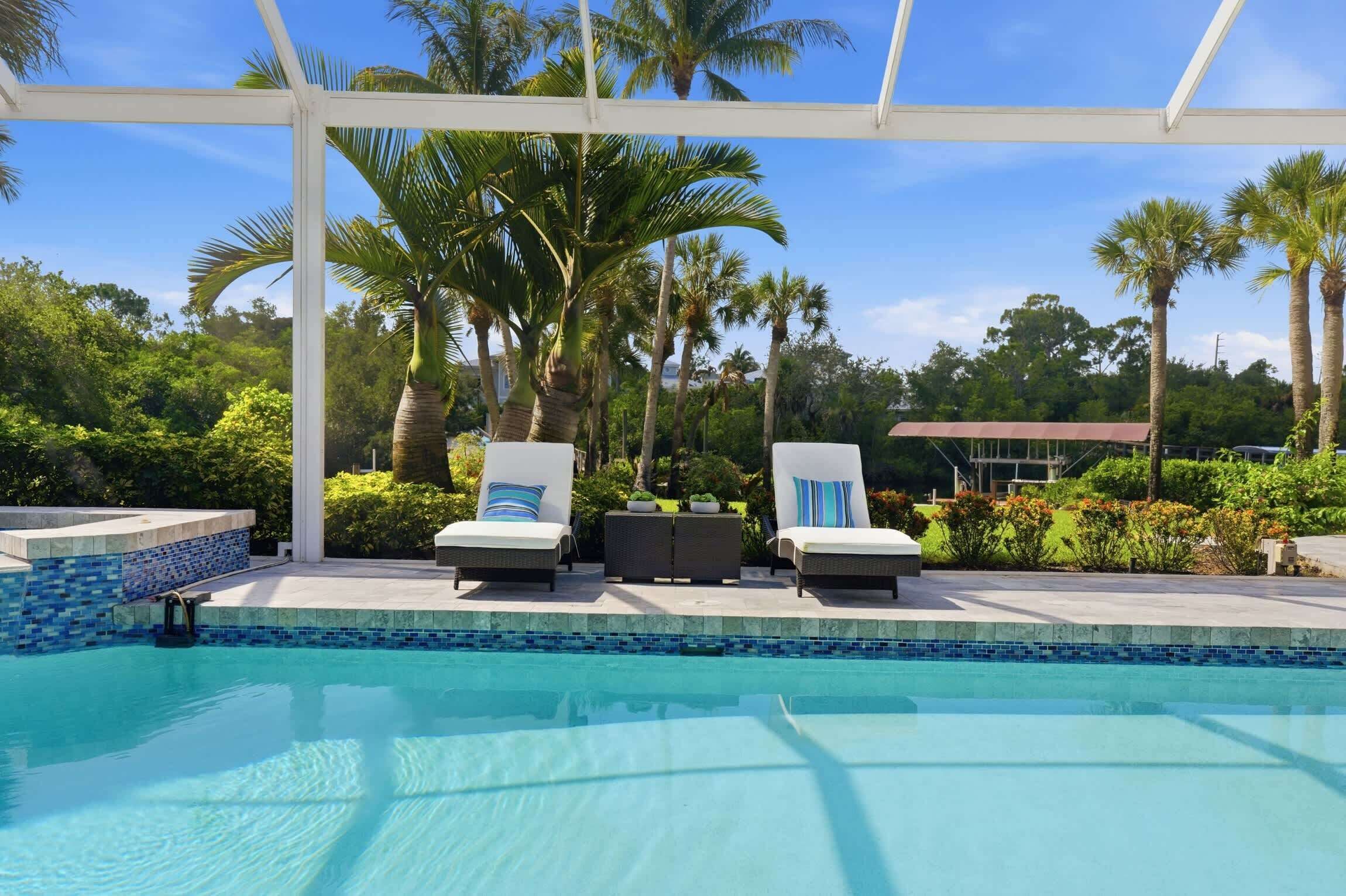 A pool area with lounge chairs, a covered seating area, and palm trees.