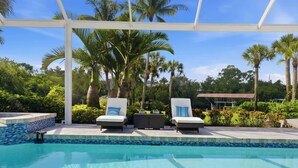A pool area with lounge chairs, a covered seating area, and palm trees. - Riverfront Retreat with Pool, Spa & Dock (Estero)