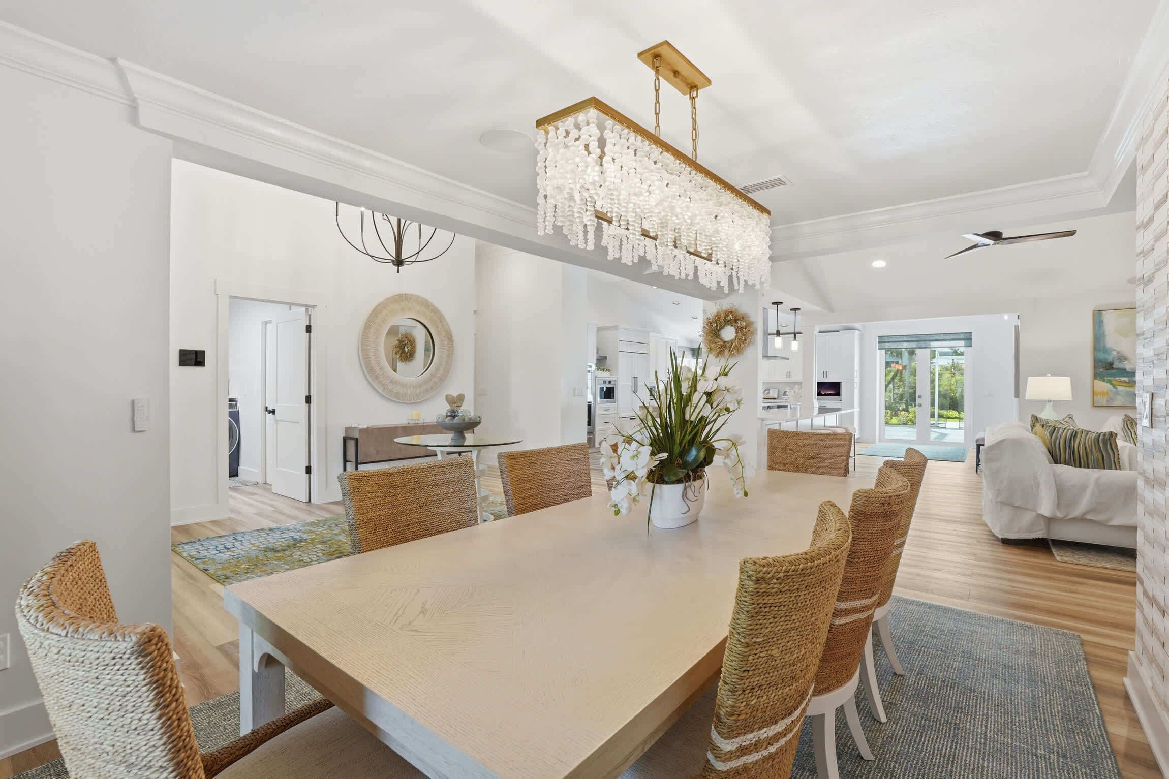A spacious dining area with a long table, wicker chairs, a chandelier, and a view into the kitchen.