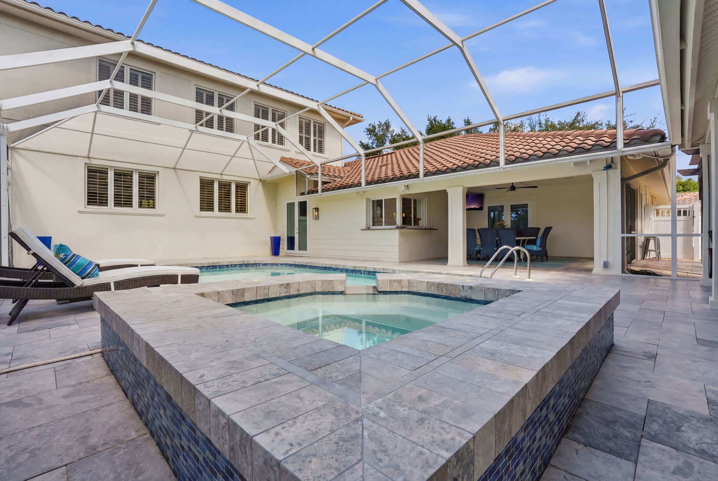 Una piscina con bordo piastrellato, un patio coperto e un'area pranzo.