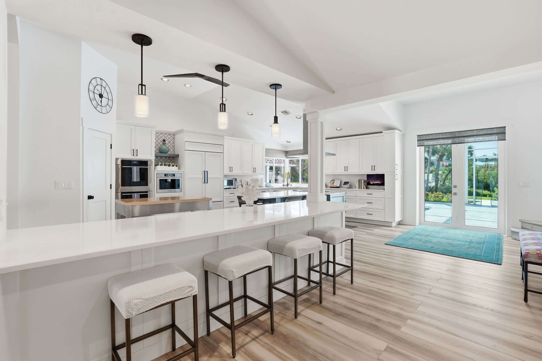 A modern kitchen with a large island, bar stools, and a view to the outside.