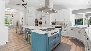 A modern kitchen with white cabinetry, a blue island, and a built-in oven. - Riverfront Retreat with Pool, Spa & Dock (Estero)