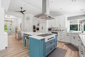 A modern kitchen with white cabinetry, a blue island, and a built-in oven. - Riverfront Retreat with Pool, Spa & Dock (Estero)