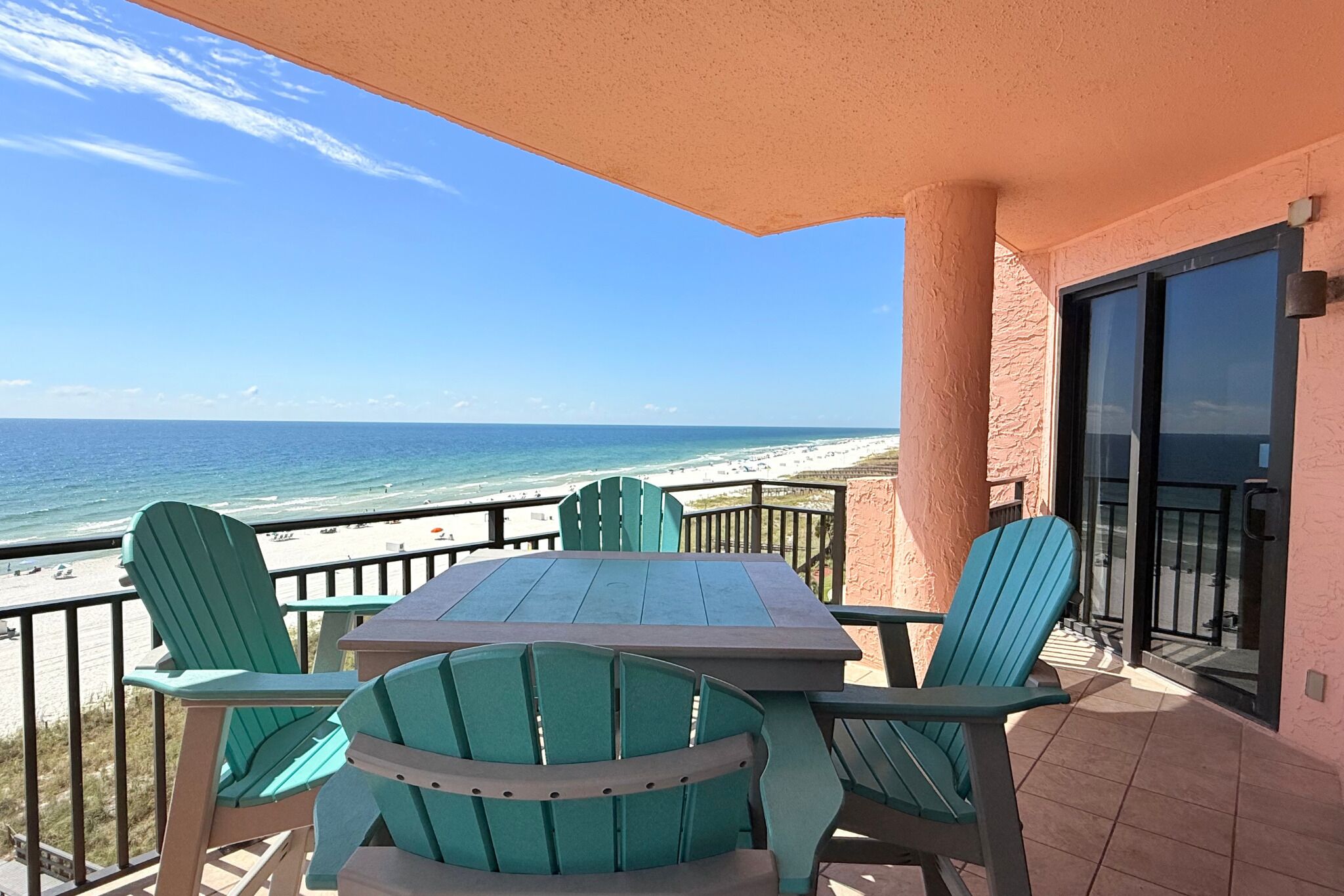 Ein Balkon mit Blick auf den Strand, ein Tisch und grüne Stühle.