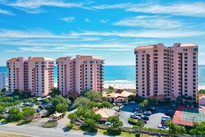 Een hoog hotel met meerdere verdiepingen, een parkeerplaats en uitzicht op het strand.