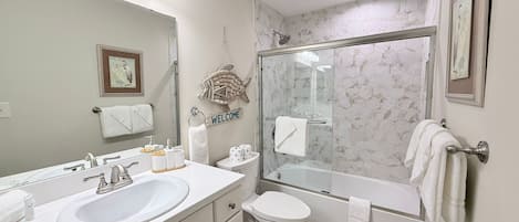 Un baño moderno con un espejo grande, un lavamanos, un inodoro y una ducha con mampara de vidrio.