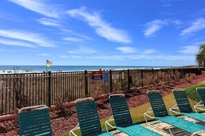 Blick auf einen Strand mit Holzzaun, Liegestühlen und einer Flagge.