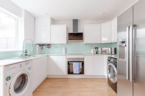 A modern kitchen with white cabinets, a washing machine, a dryer, and a microwave. - Large Modern 4 BDR Home Near ExCel London (Greater London)