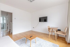 A modern living room with a flat-screen TV mounted on the wall, a wooden coffee table, and a dining area with a table and chairs. - Large Modern 4 BDR Home Near ExCel London (Greater London)