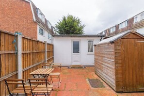 A backyard with a wooden fence, a shed, and a door leading to a small white building. - Large Modern 4 BDR Home Near ExCel London (Greater London)