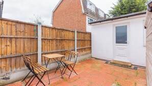 A backyard with a wooden fence, a small shed, and a patio table with chairs. - Large Modern 4 BDR Home Near ExCel London (Greater London)