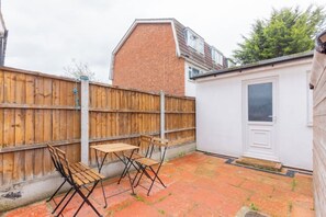 A backyard with a wooden fence, a small shed, and a patio table with chairs. - Large Modern 4 BDR Home Near ExCel London (Greater London)