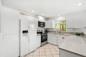 A modern kitchen with white cabinets, stainless steel appliances, and a window with a view of greenery. - 217 Cherie Down Ln (Cape Canaveral)