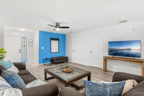 A living room with a sofa, coffee table, TV, and a ceiling fan. - 217 Cherie Down Ln (Cape Canaveral)
