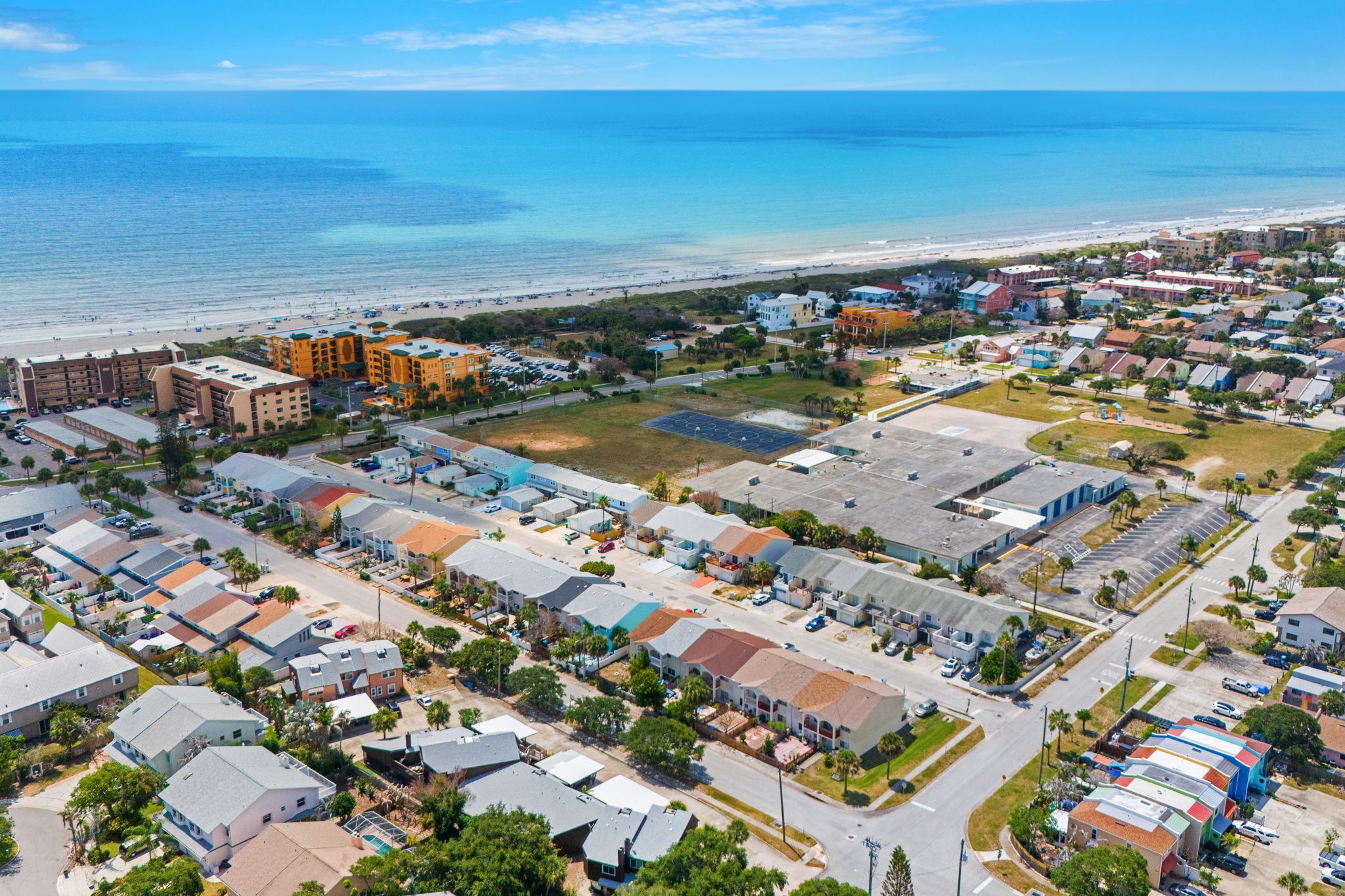 An aerial view of a coastal town with residential buildings, a beach, and a marina.