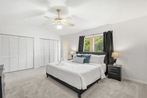 A bedroom with a bed, nightstands, a ceiling fan, and a view of greenery outside. - 217 Cherie Down Ln (Cape Canaveral)
