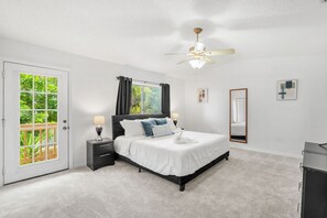 A bedroom with a bed, a nightstand, a ceiling fan, a window with curtains, and a door. - 217 Cherie Down Ln (Cape Canaveral)