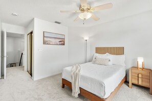 A bedroom with a bed, bedside table, nightstand, ceiling fan, and a painting on the wall. - 217 Cherie Down Ln (Cape Canaveral)