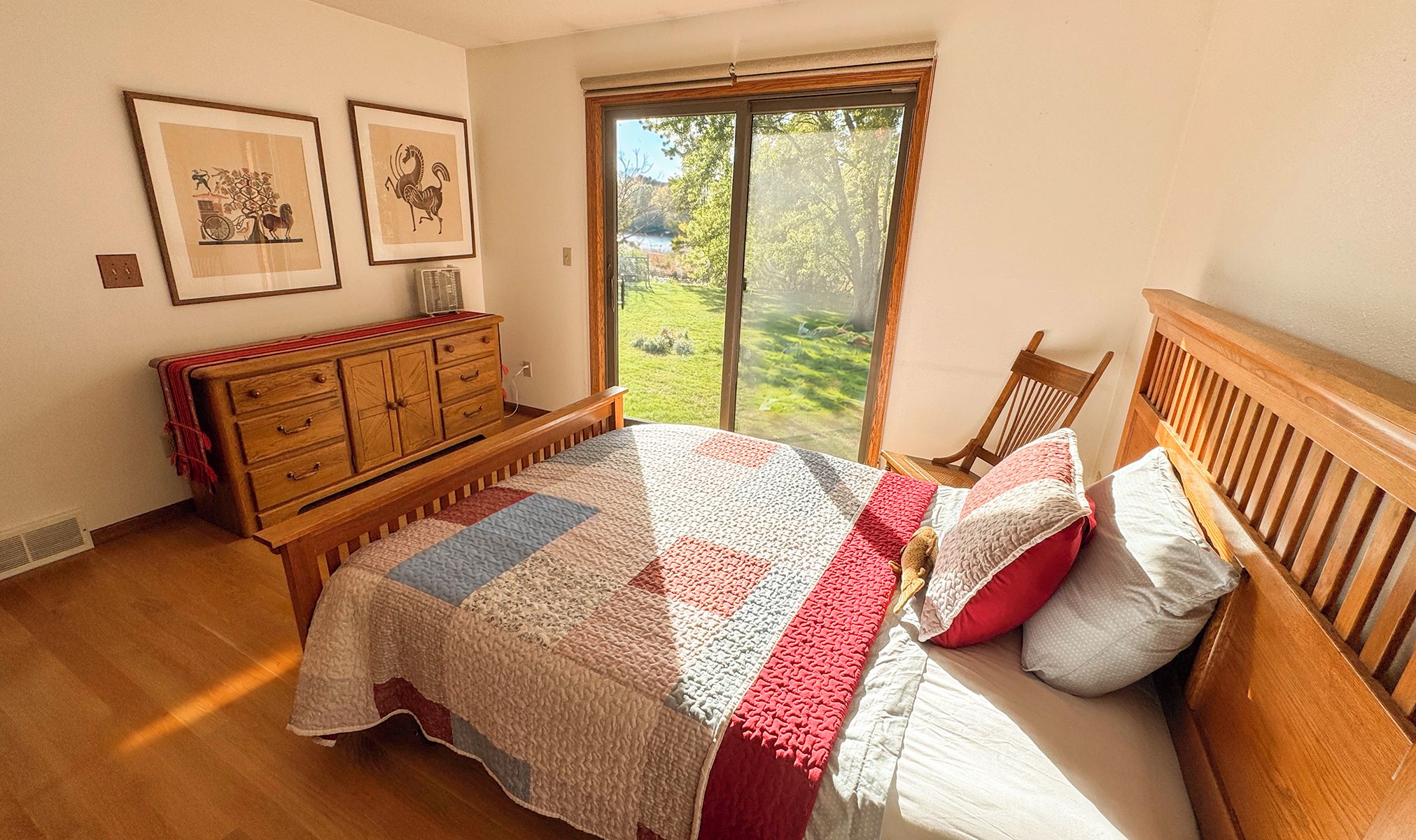 Un dormitorio con una cama grande, un aparador de madera y una ventana con vistas a follaje.