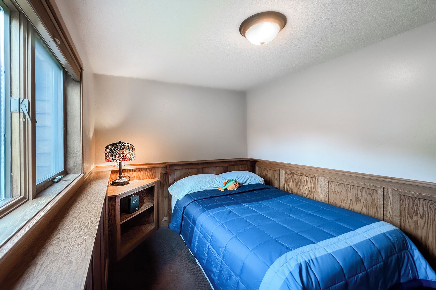 A bedroom with a bed, a nightstand, a lamp, and a window.