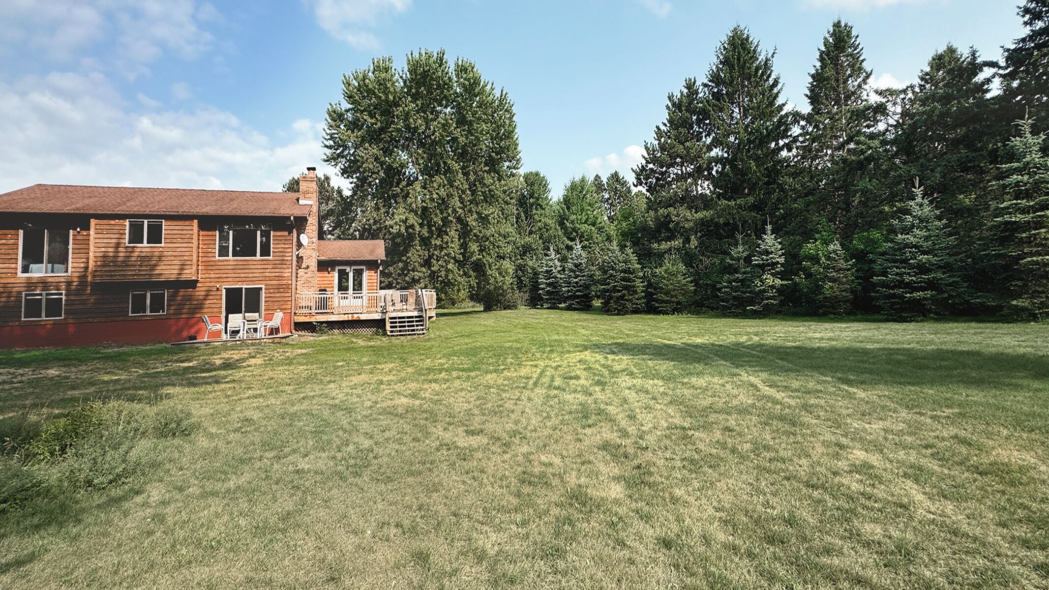 A two-story wooden house with a deck and a large grassy yard.