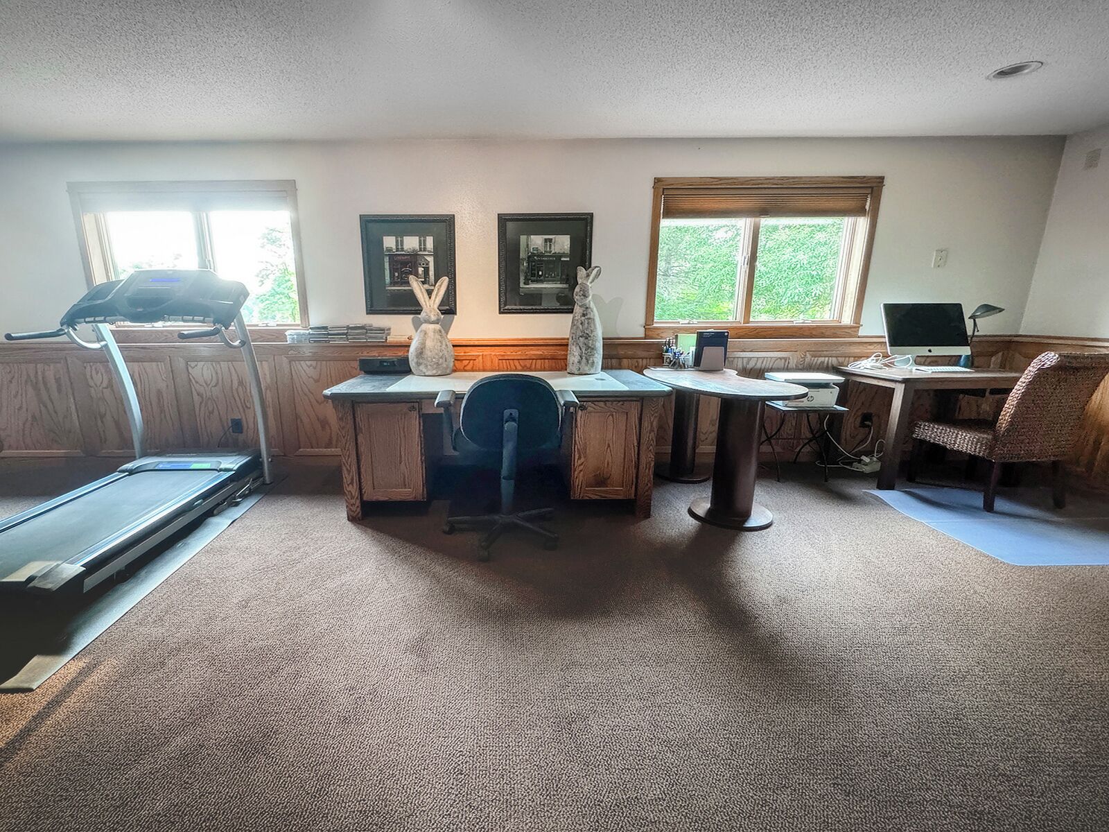 A room with a treadmill, a desk, a computer, and a chair.