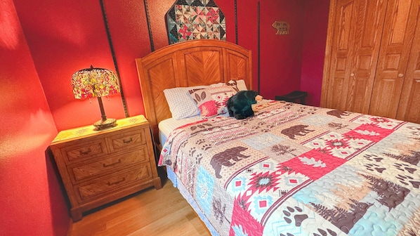 A bedroom with a wooden bed, a nightstand with a lamp, and a quilt with animal patterns.