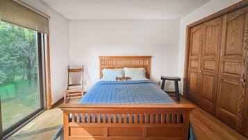 A bedroom with a wooden bed, a chair, a small stool, and a wardrobe.