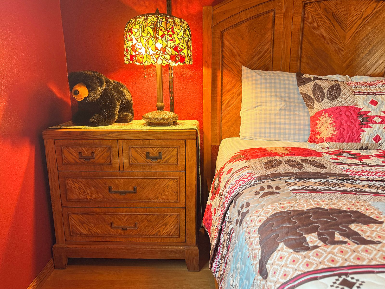 Une table de chevet en bois, dotée de tiroirs, une lampe et un ours en peluche.