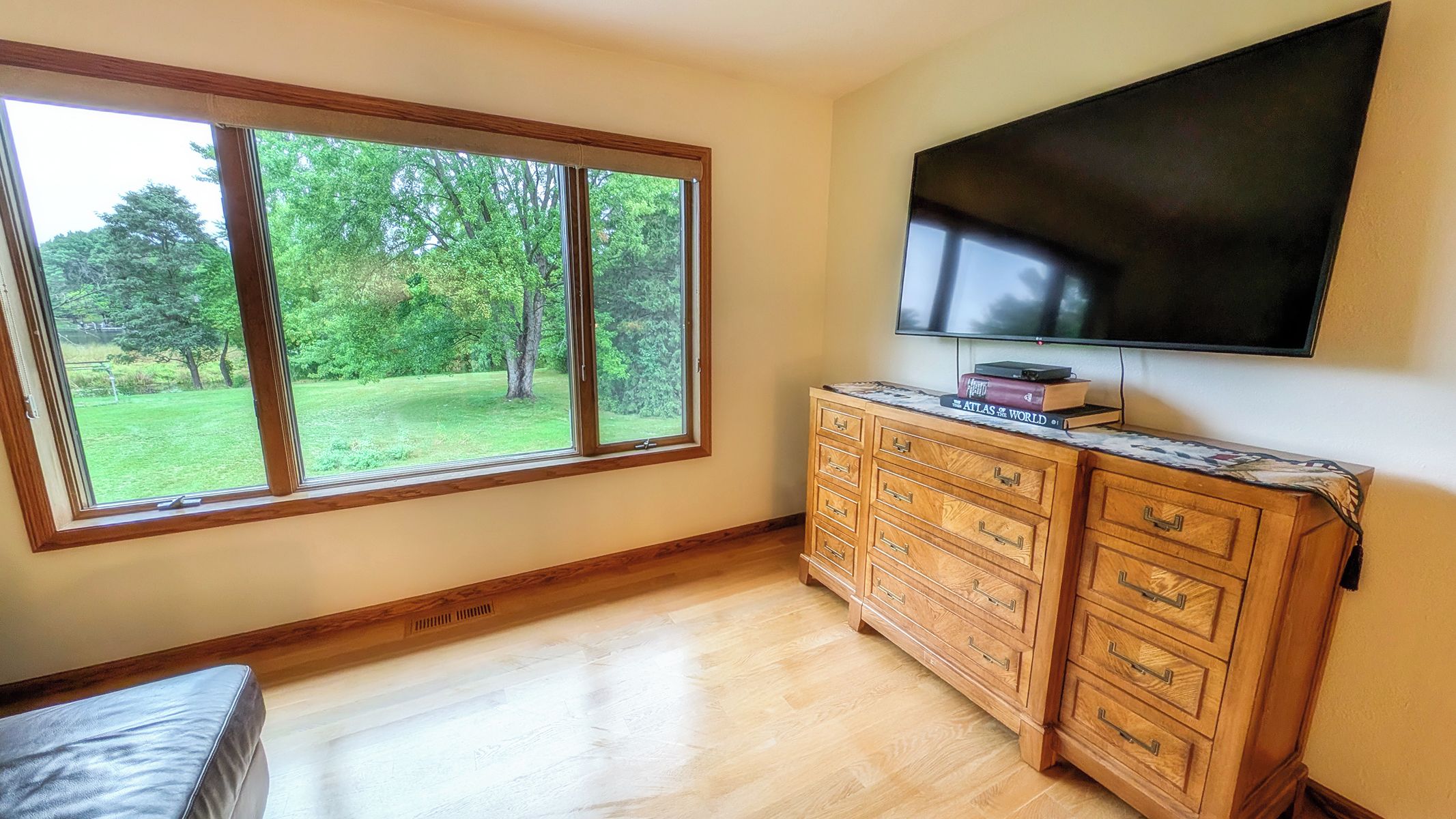 A room with a large window, a flat-screen TV, and a wooden cabinet.