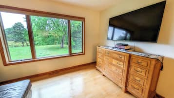 A room with a large window, a flat-screen TV, and a wooden cabinet.