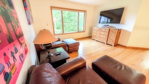 A living room with leather sofas, a lamp, a TV, and a window with a view of trees.