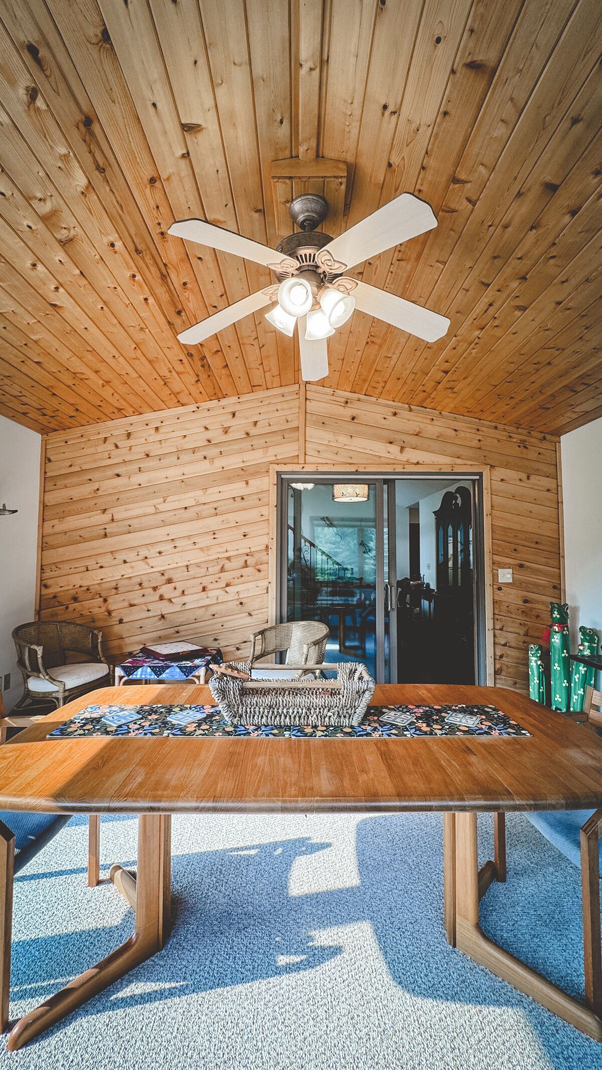 A wooden interior with a ceiling fan, a dining table, and a view through a glass door.