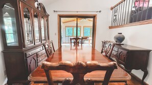 A long wooden dining table with ornate chairs, flanked by wooden cabinets with glass doors, in a room with a view of the outdoors.