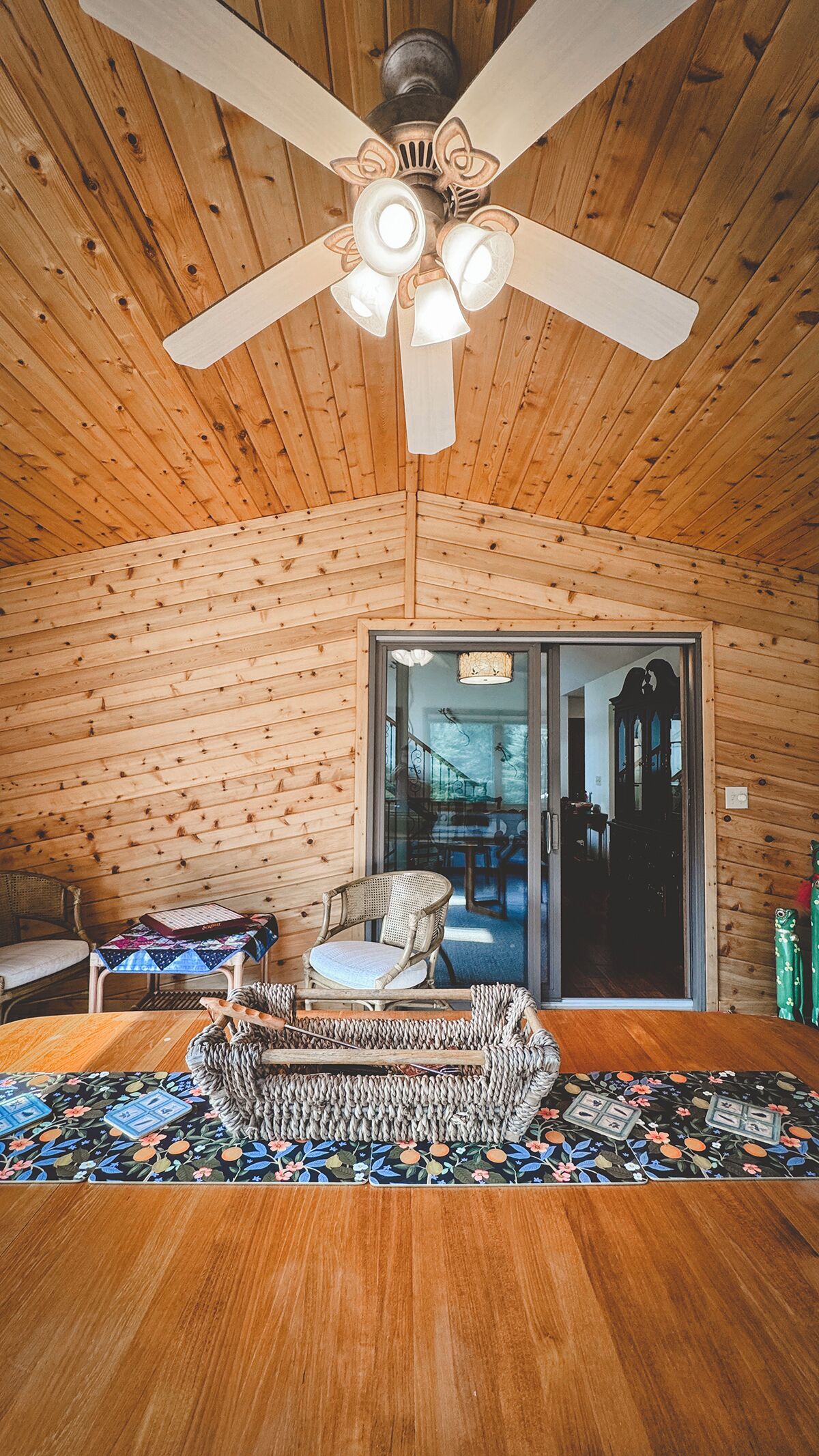 A wooden interior with a ceiling fan, a woven rug, and a view through a glass door to another room.