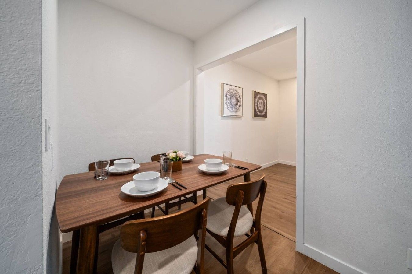 A dining area with a wooden table set for four, white plates, and a vase with flowers.