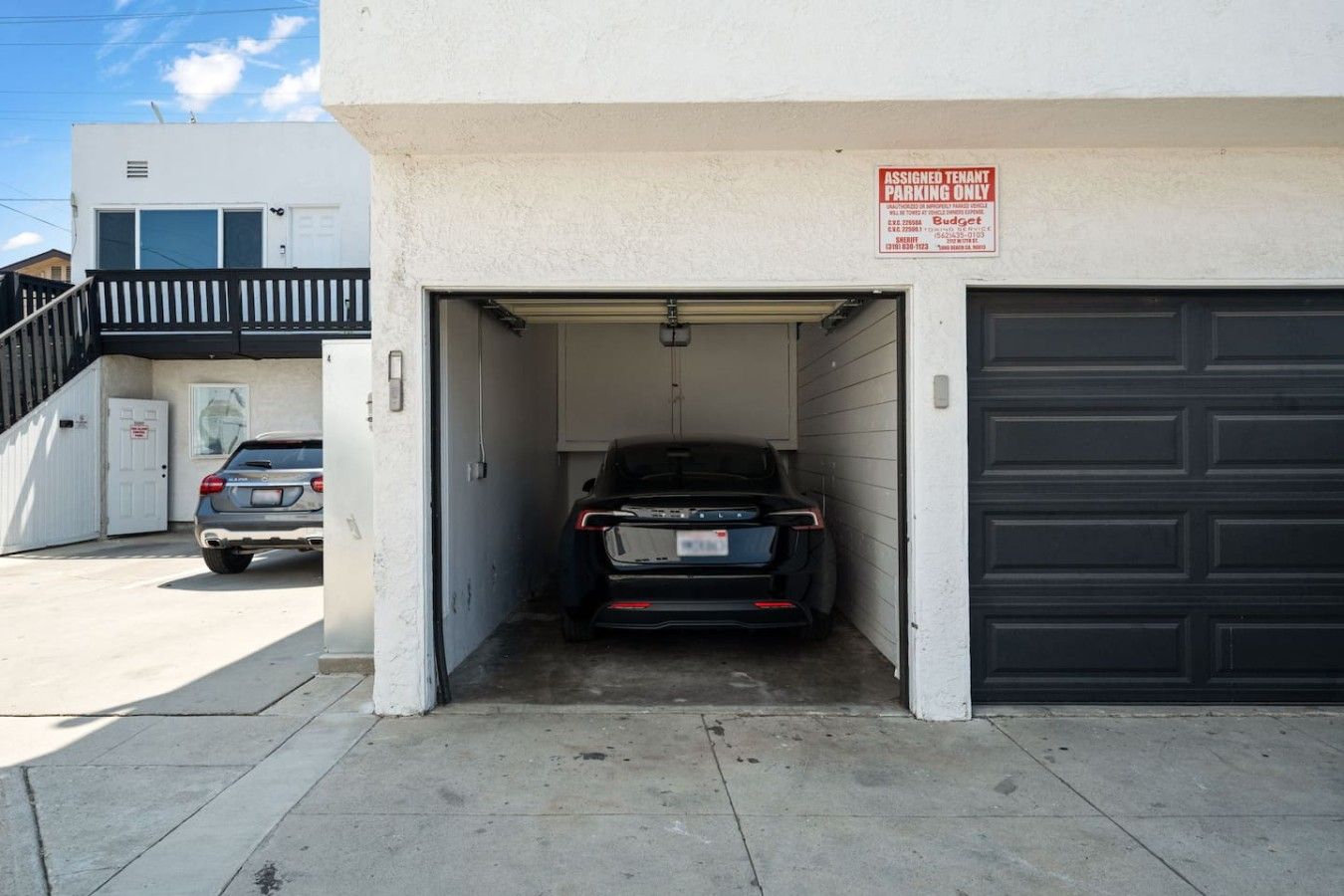 A garage with a black SUV parked inside, a white building with a black garage door, and a sign indicating 'Assigned Tenant Parking Only.'
