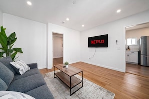 Un salón moderno con un sofá gris, una mesa de centro y un televisor instalado en la pared mostrando 'NETFLIX'.