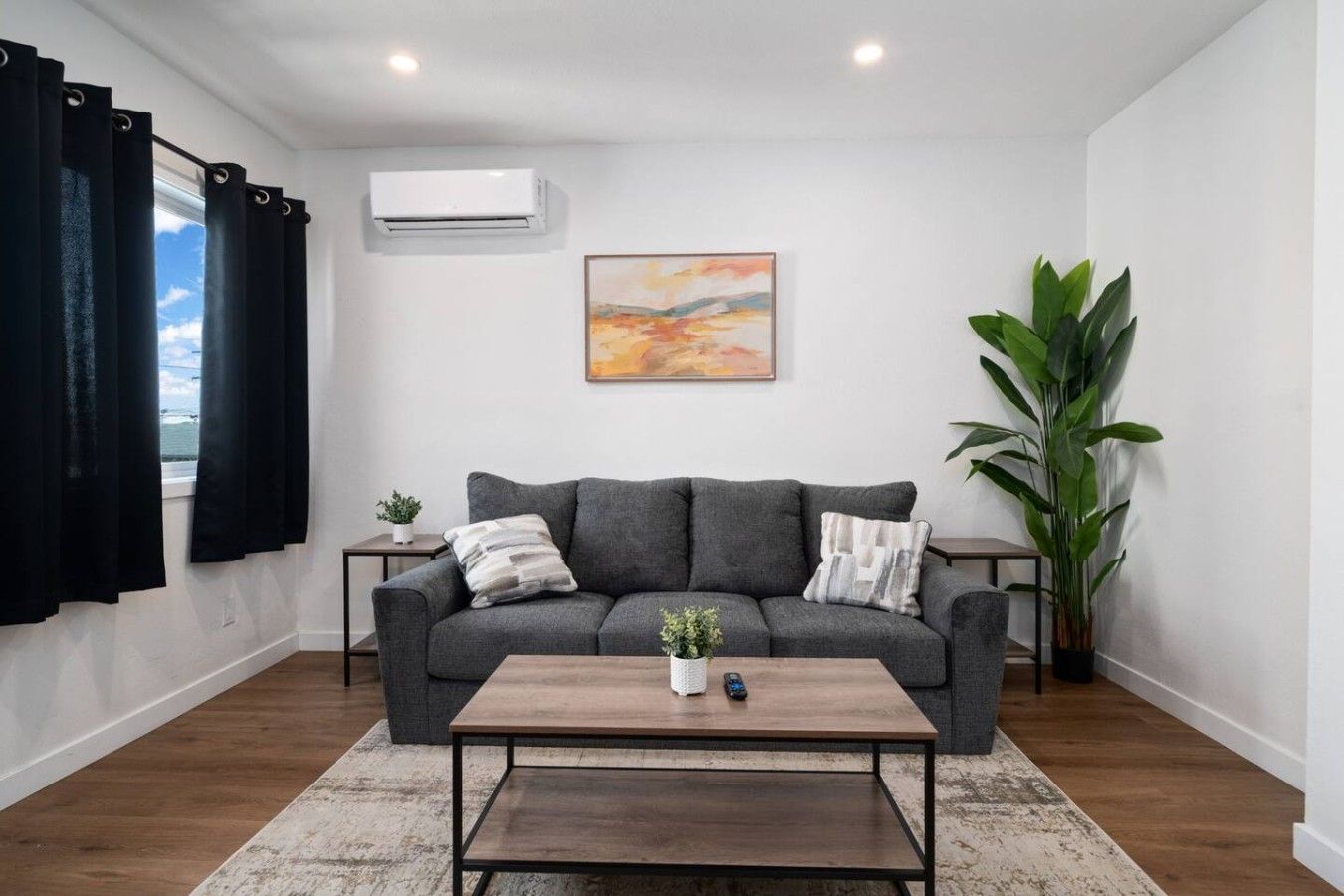 A living room with a grey sofa, a coffee table, a painting, and a potted plant.