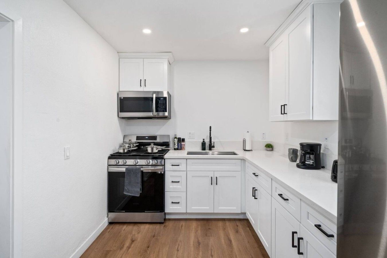 A compact kitchen with white cabinetry, a stainless steel stove, a microwave, and a refrigerator.