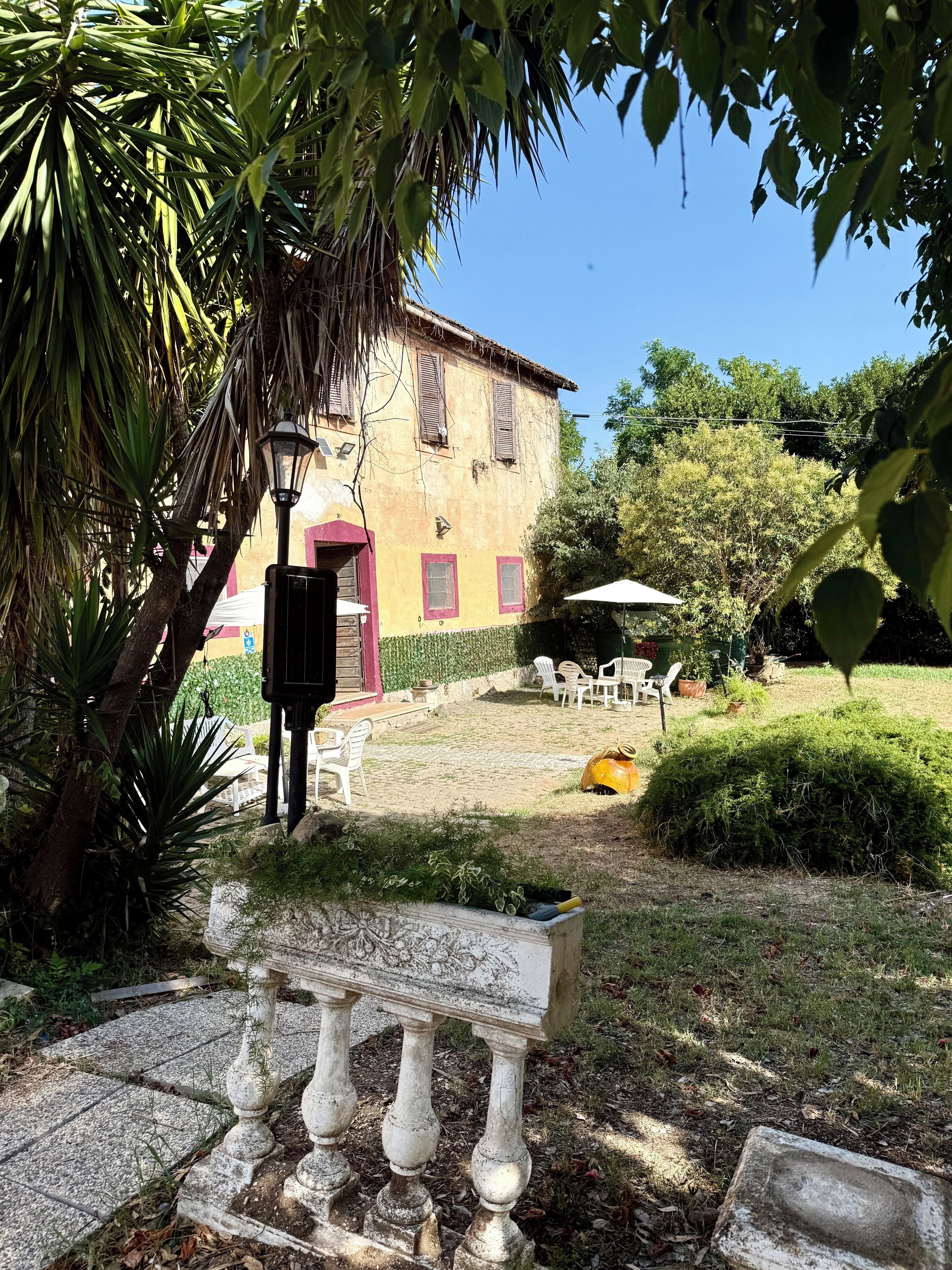 A courtyard with a stone bench, outdoor furniture, and a building with shutters.